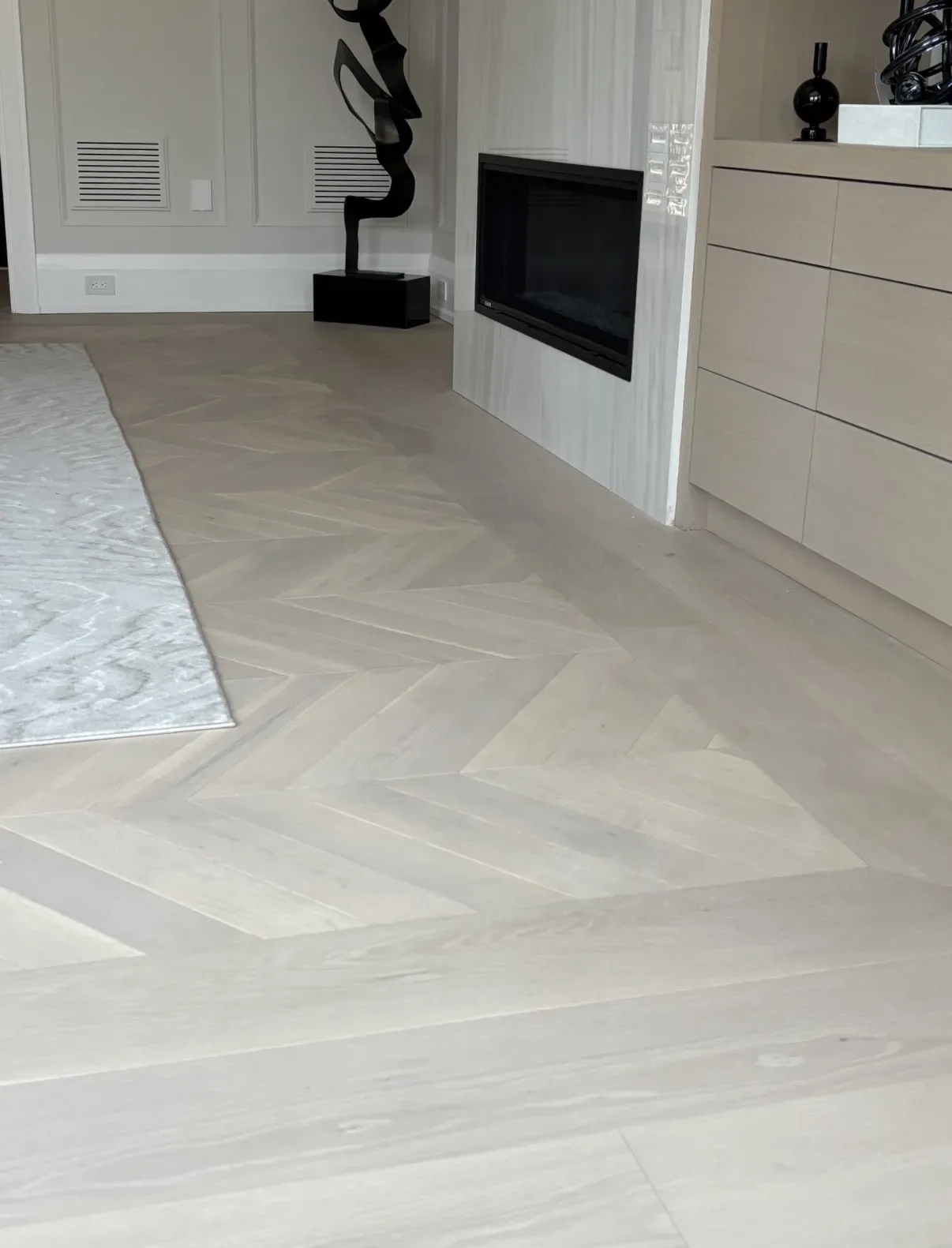 Herringbone flooring beside a fireplace and white built-in cabinetry