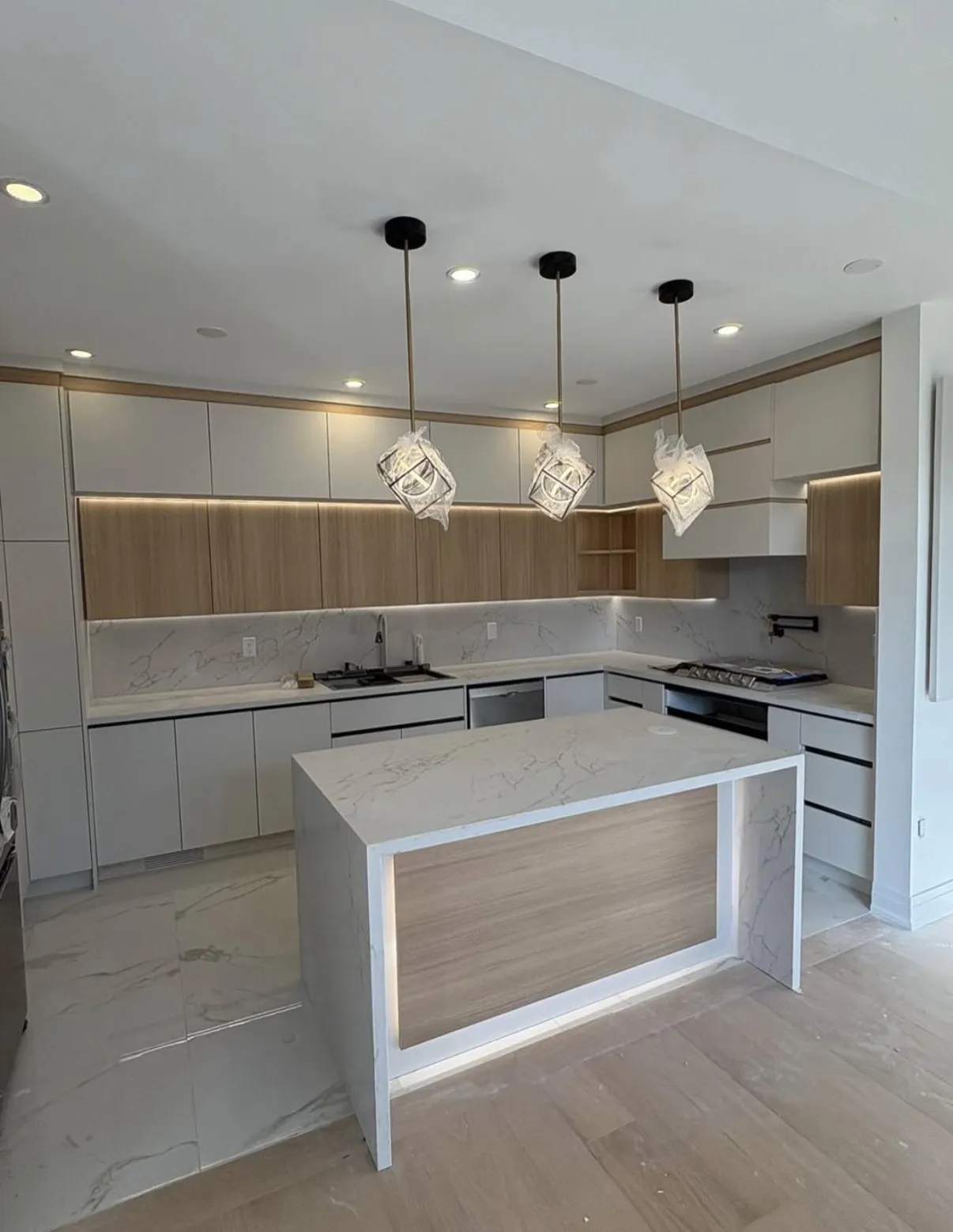 Pale kitchen island with a wood inset, geometric pendant lights and two-tone cabinetry
