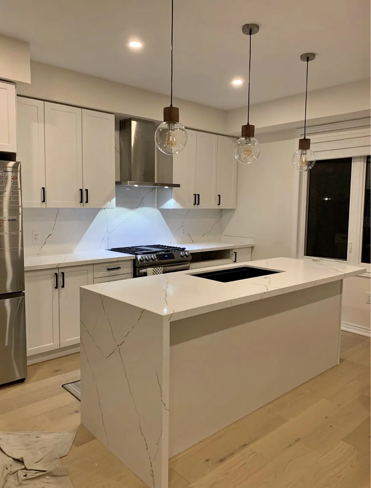 Light kitchen worktop wrapping the sides of an island beneath pendant lighting